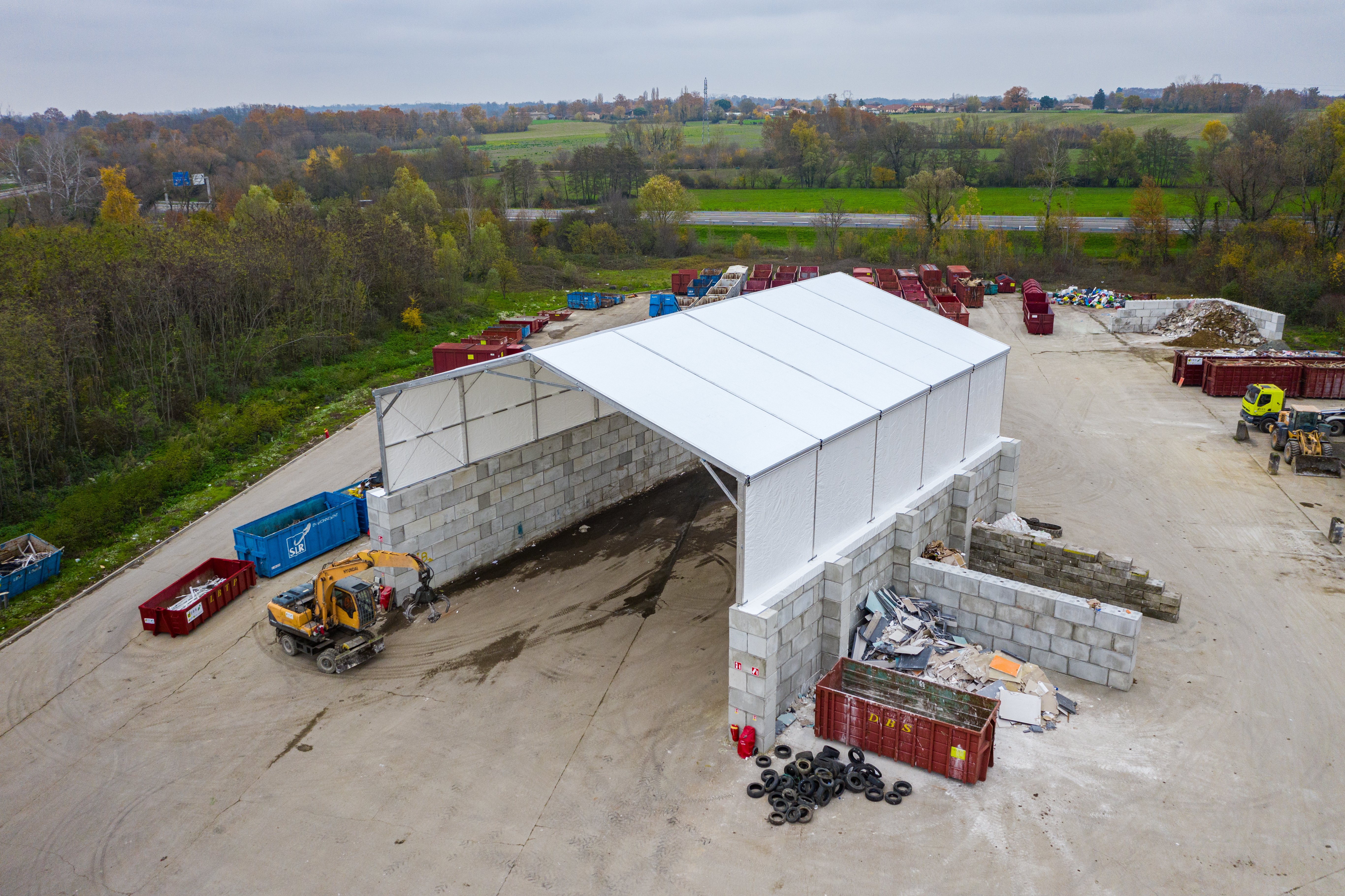 Hangar industriel démontable avec murs en blocs béton modulaires type LEGO et toiture double pente pour activité logistique